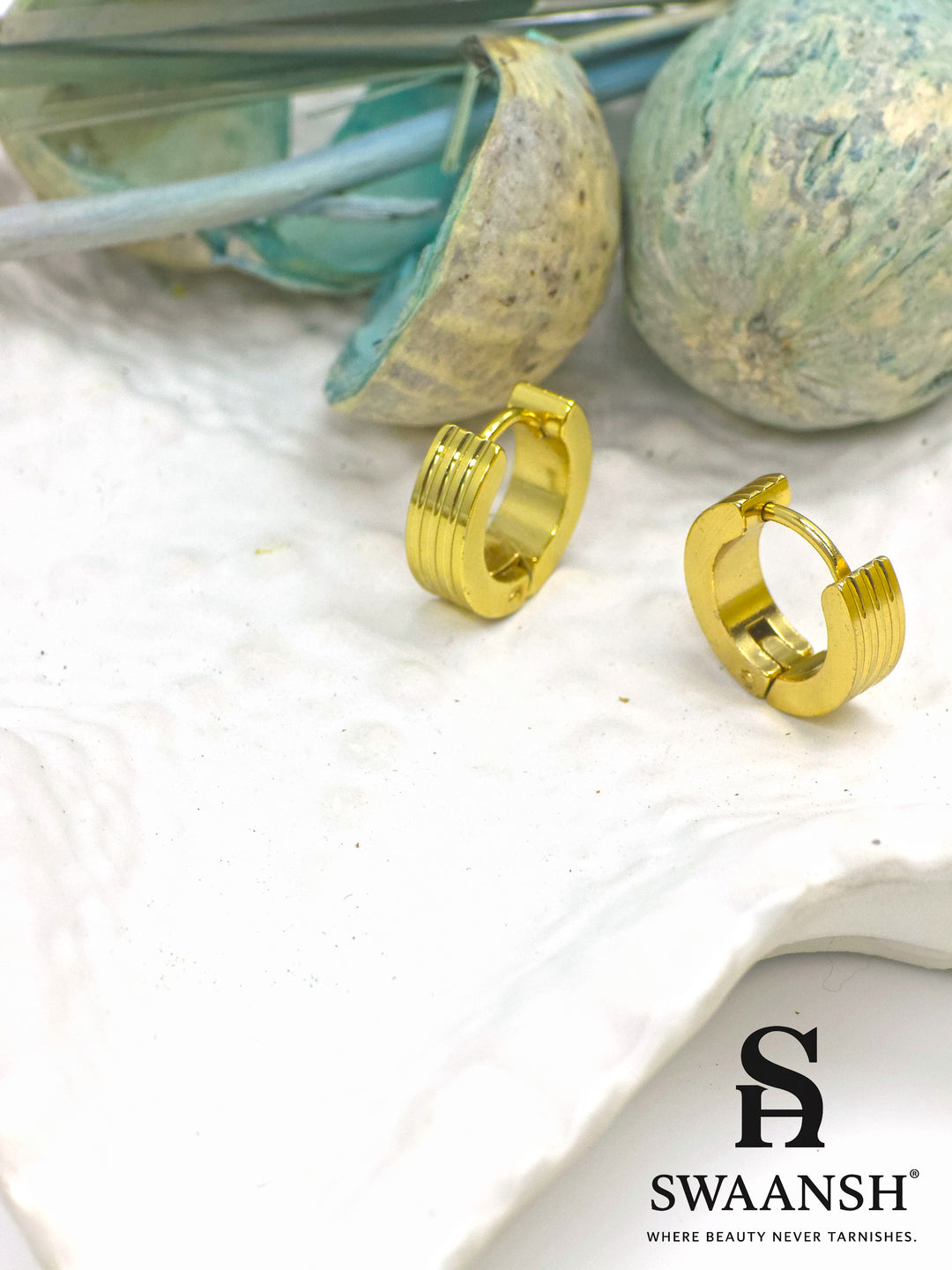 Urban Stride gold hoop earrings by Swaansh with engraved ridges and matte finish placed beside white floral accents