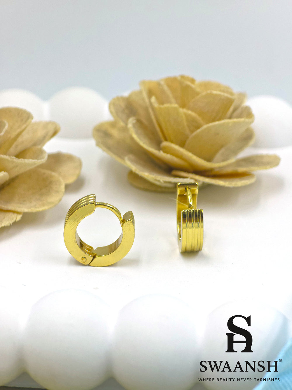Urban Stride gold hoop earrings by Swaansh with engraved ridges and matte finish placed beside white floral accents