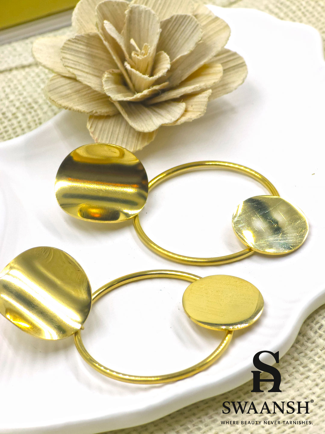Orbit Drop sculptural gold earrings by Swaansh with dual discs and open hoop design styled on a white plate