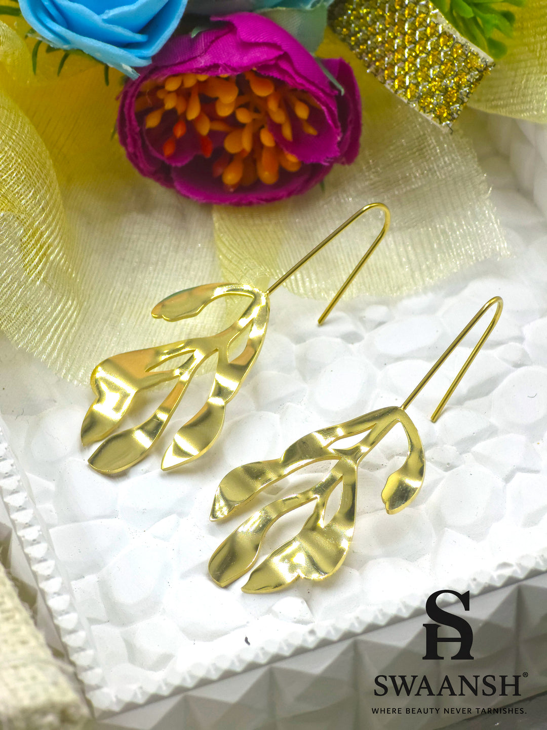 Leaf Muse gold sculptural earrings in open leaf design with artistic hook-back by Swaansh, styled on a white plate with beige flowers
