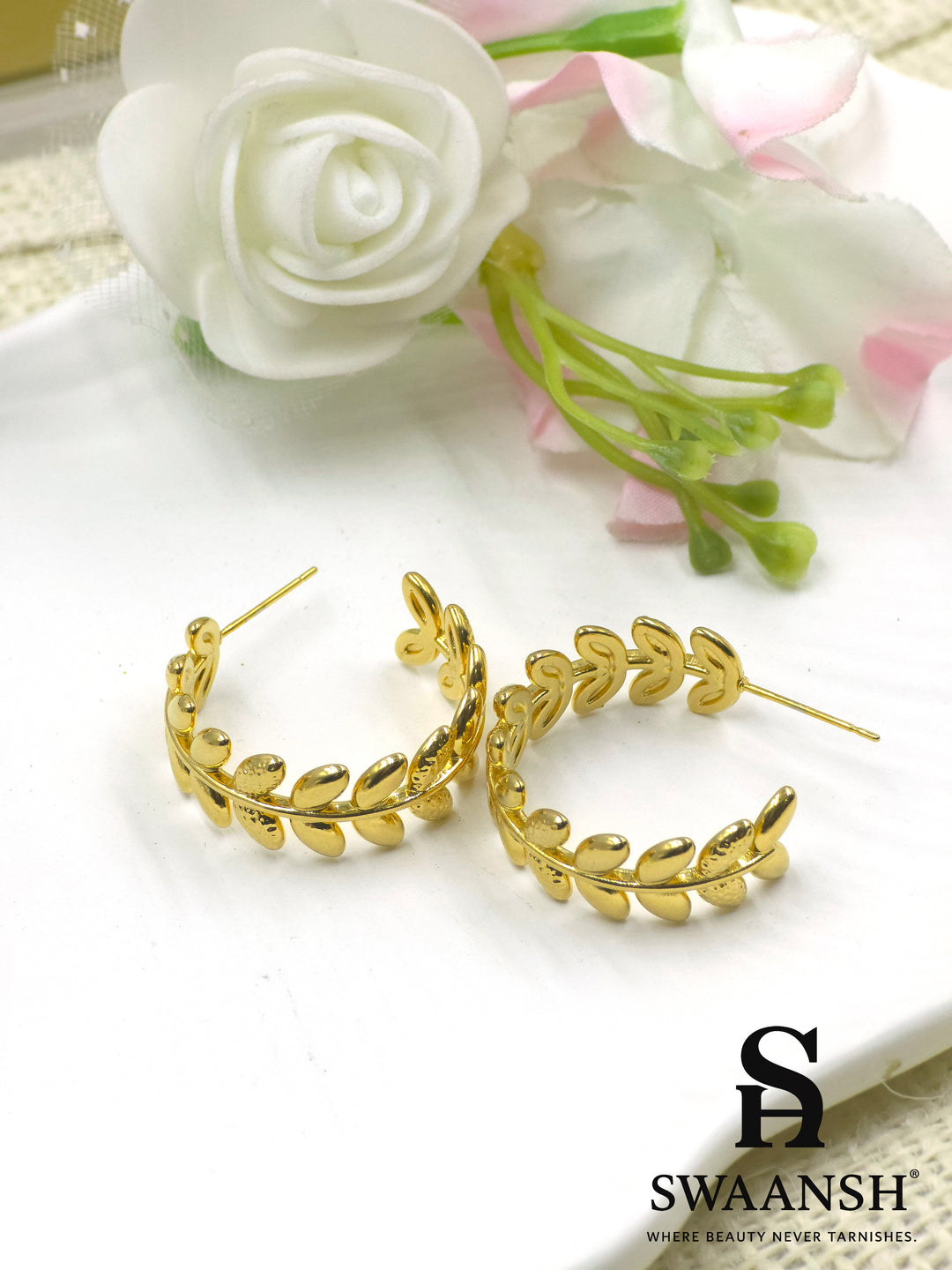 Swaansh Golden Laurel earrings – gold hoop earrings with delicate laurel leaf design, placed on a white plate with floral background