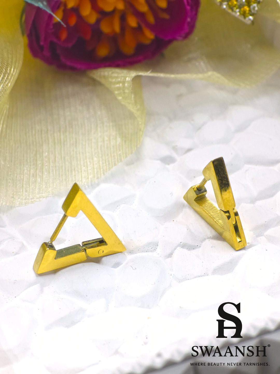 Swaansh GeoGlam triangle hoop earrings in gold placed on white ceramic plate with pastel floral decor
