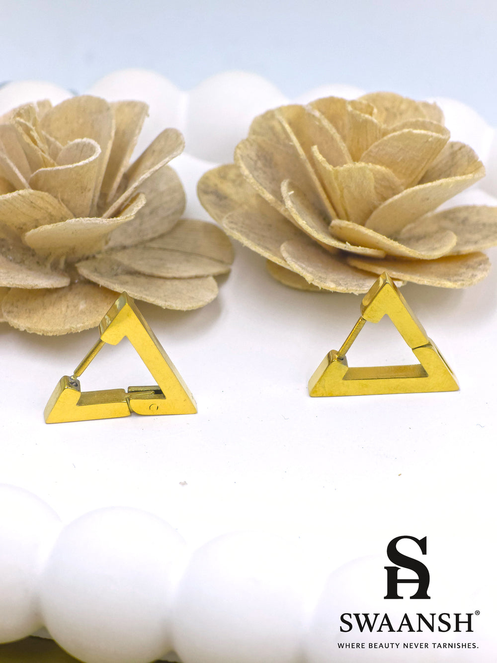 Swaansh GeoGlam triangle hoop earrings in gold placed on white ceramic plate with pastel floral decor