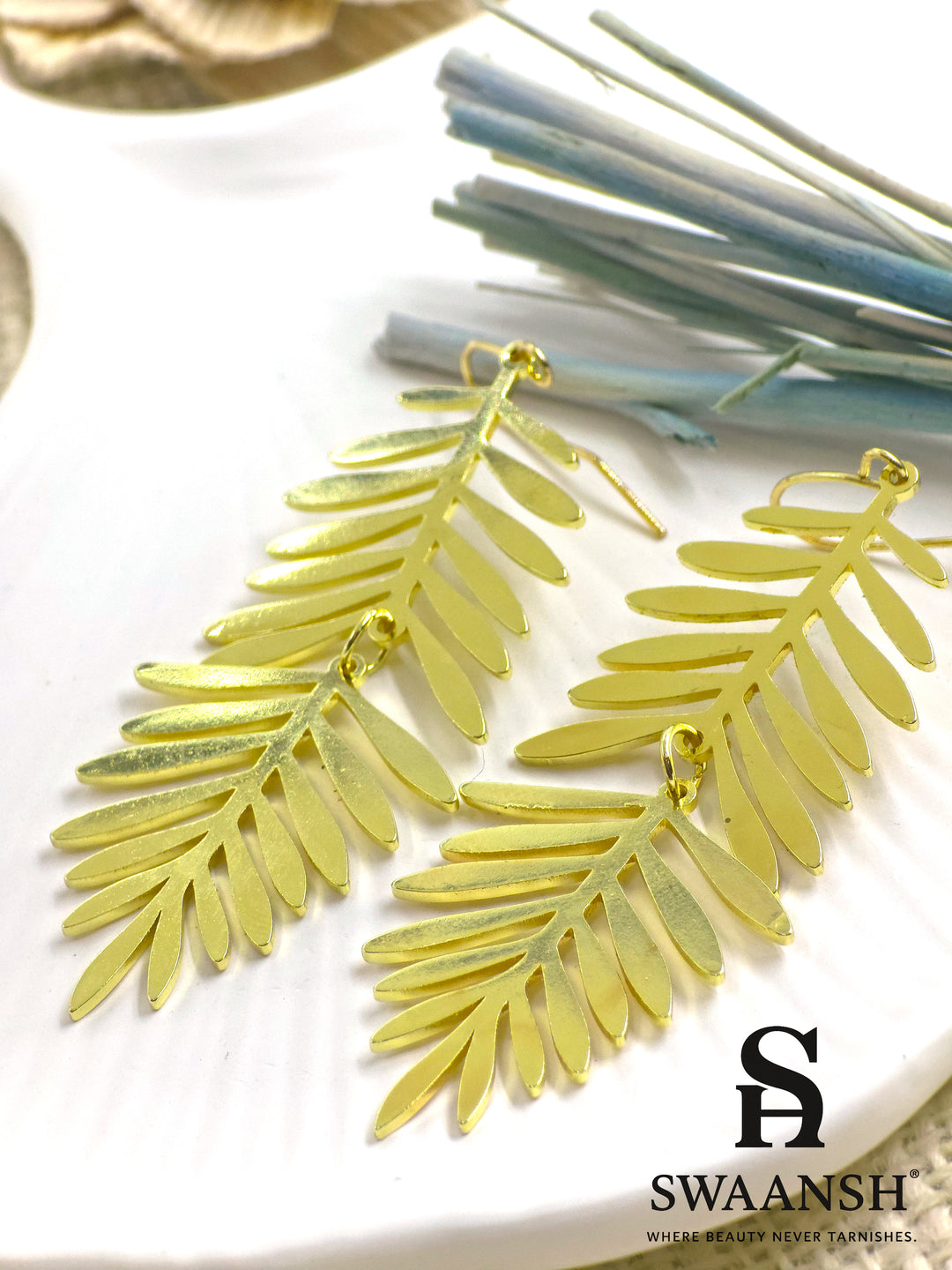 PalmWhisper – tropical palm leaf gold earrings styled on a white ceramic plate with dried flowers in background