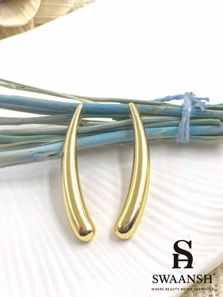 SwayDrop sleek curved gold earrings placed on a white ceramic plate with dried blue floral accents – premium anti-tarnish jewellery by Swaansh