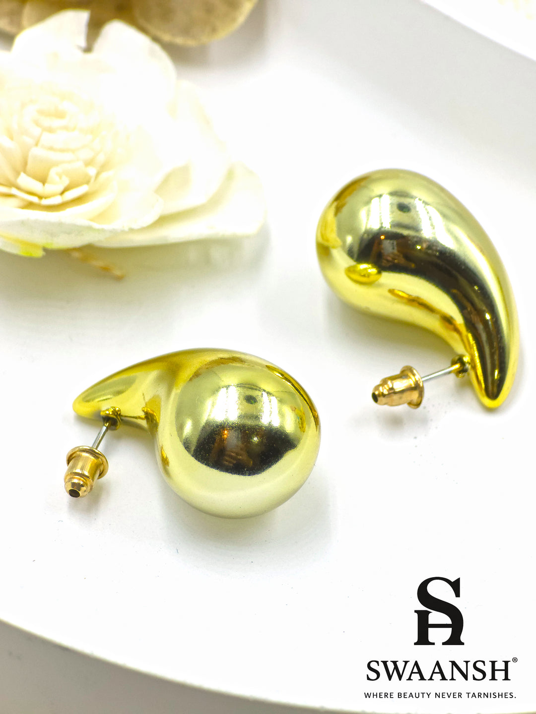 Molten Drop earrings by Swaansh in fluid sculptural design with glossy gold finish, displayed on floral ceramic background