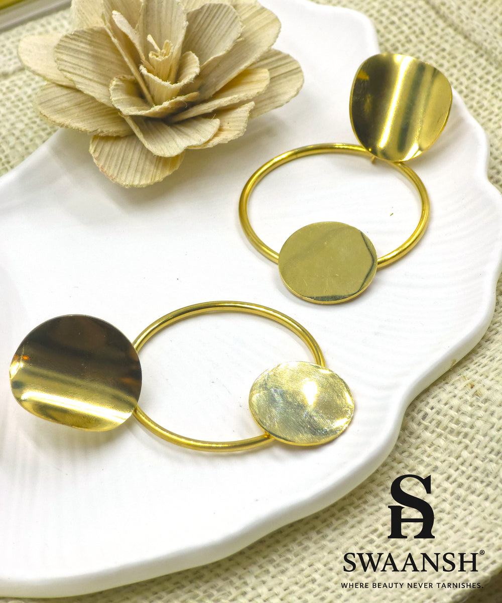 Orbit Drop sculptural gold earrings by Swaansh with dual discs and open hoop design styled on a white plate