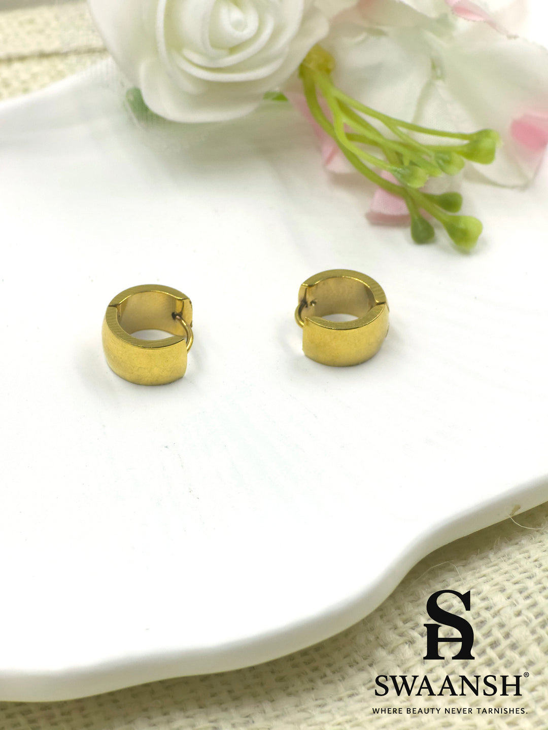 Swaansh Urban Edge matte gold huggie hoop earrings placed on white ceramic plate with floral decor in background
