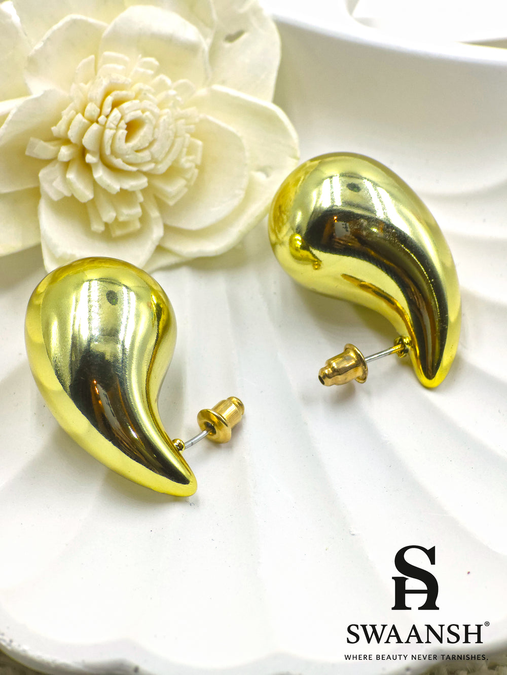 Molten Drop earrings by Swaansh in fluid sculptural design with glossy gold finish, displayed on floral ceramic background