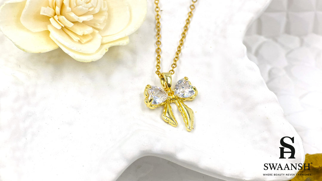 Twilight Bow Pendant by Swaansh featuring crystal heart accents tied in a sculpted gold ribbon on a delicate chain